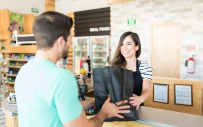 Confident female cashier giving bag to young man at checkout counter in supermarket